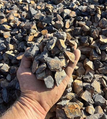 Ballast rock in hand hovering above large pile of material